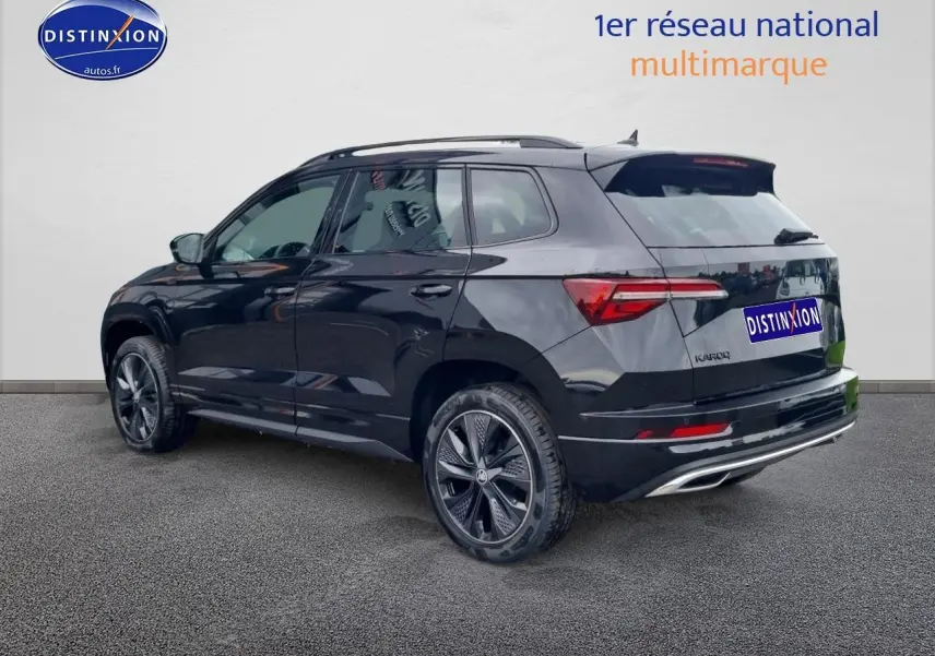 SKODA KAROQ noir 2025 en 3/4 arrière droit, avec jantes alu et barres de toit visibles.