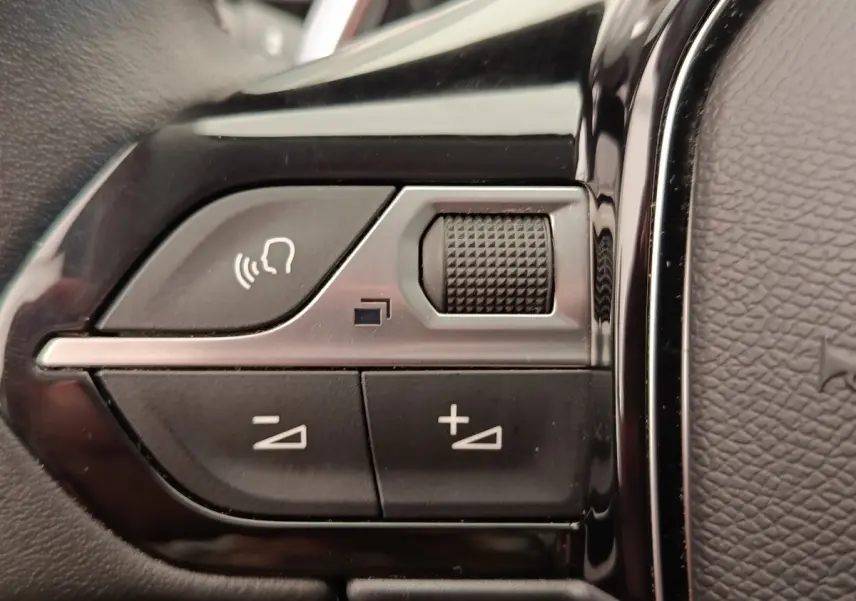 Gros plan sur les commandes vocales et volume au volant cuir noir du Peugeot 5008 gris foncé, version 2020.