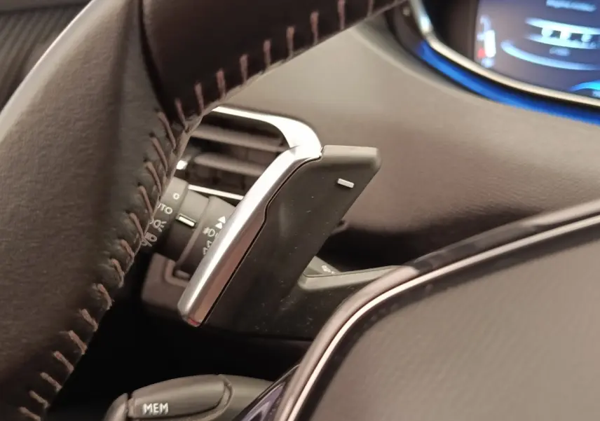Gros plan sur la palette de changement de vitesse derrière le volant cuir d'une Peugeot 5008 gris foncé, tableau de bord partiellement visible.