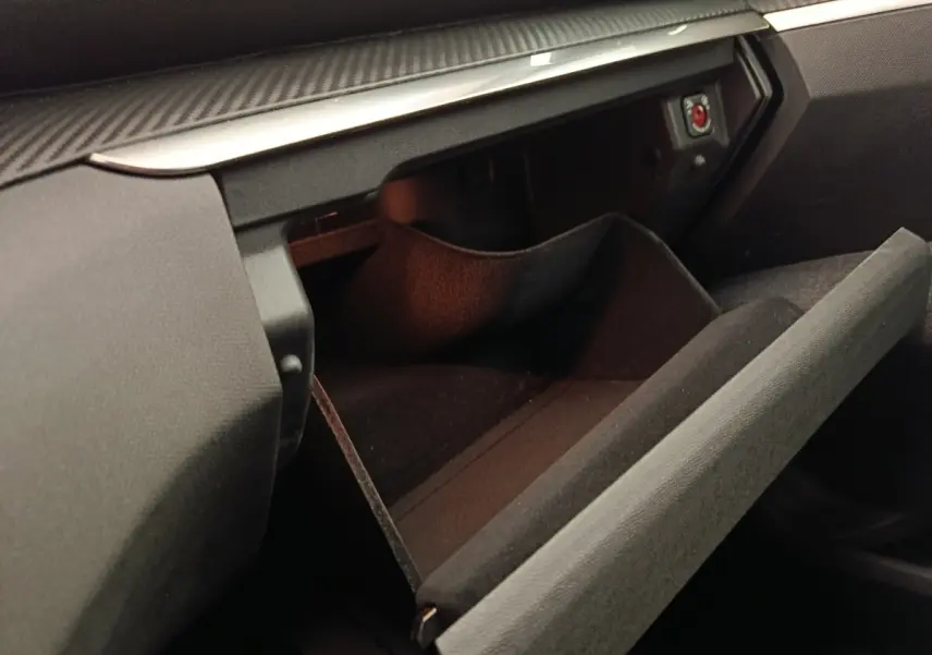 Gros plan sur la boîte à gants ouverte côté passager du Peugeot 5008 gris foncé, intérieur noir et détails en carbone.