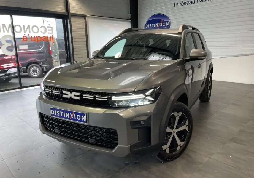 Vue 3/4 avant du Dacia Bigster gris schiste avec calandre noire et jantes alliage bicolores dans un showroom.