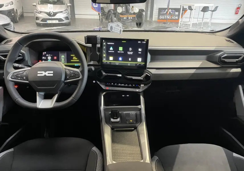 Vue intérieure avant du tableau de bord et volant du Dacia Bigster gris schiste avec écran tactile central et commandes au volant.
