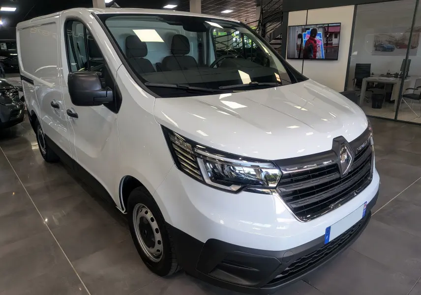 Vue 3/4 avant gauche d’un Renault Trafic Fourgon blanc minéral 2024 avec calandre noire et phares modernes.