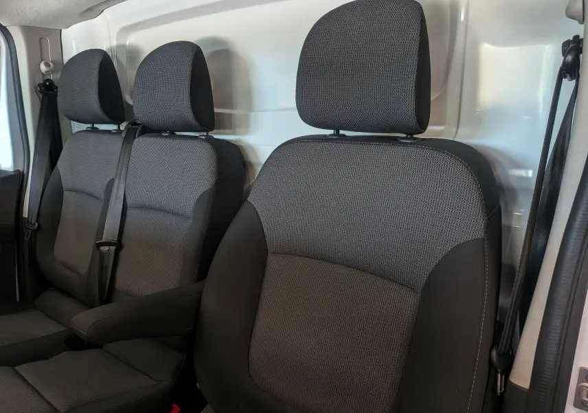 Vue intérieure des sièges avant en tissu gris foncé du Renault Trafic Fourgon 2024, avec cloison métallique blanche en arrière-plan.