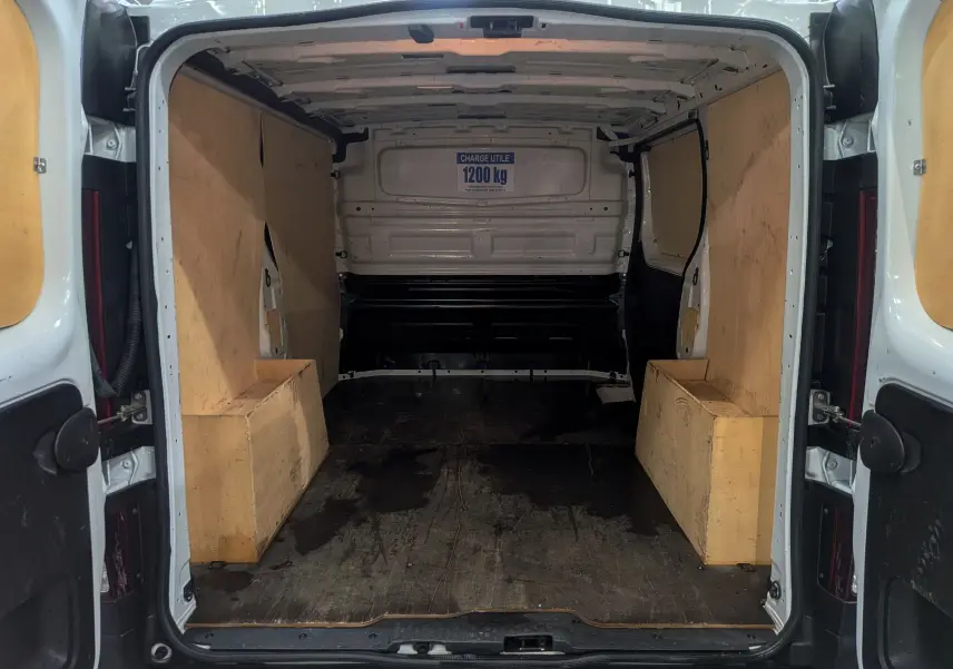 Intérieur du coffre du Renault Trafic Fourgon blanc minéral, vue arrière ouverte montrant l'espace de chargement avec panneaux en bois.