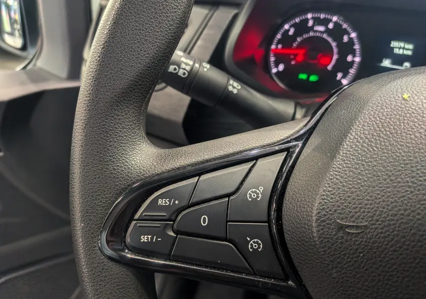 Gros plan sur les commandes de régulateur de vitesse au volant noir du Renault Trafic Fourgon 2024, tableau de bord en arrière-plan.