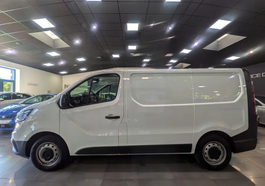 Vue de profil côté gauche d’un Renault Trafic Fourgon blanc minéral 2024 en intérieur, avec jantes acier et poignées noires.
