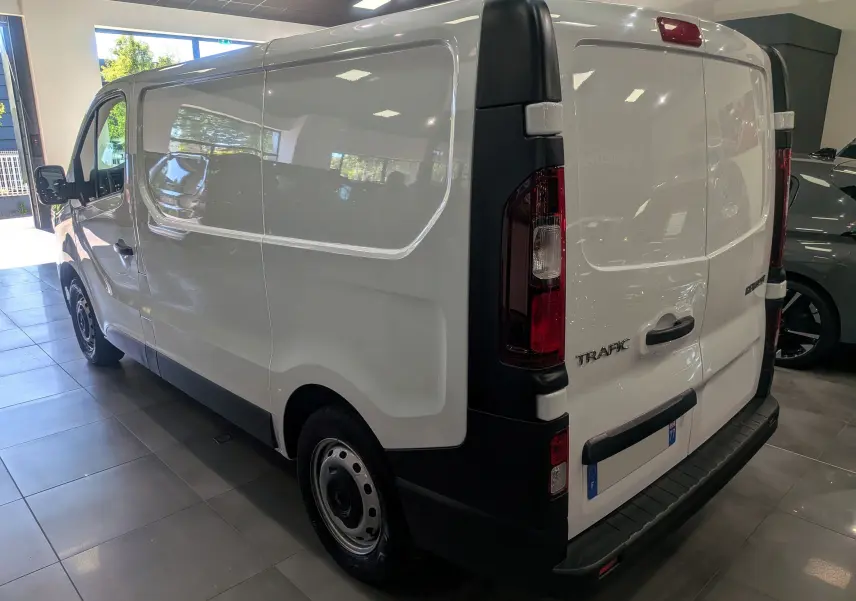 Vue 3/4 arrière droite d’un Renault Trafic Fourgon blanc minéral 2024, avec portes arrière fermées et jantes acier noires.