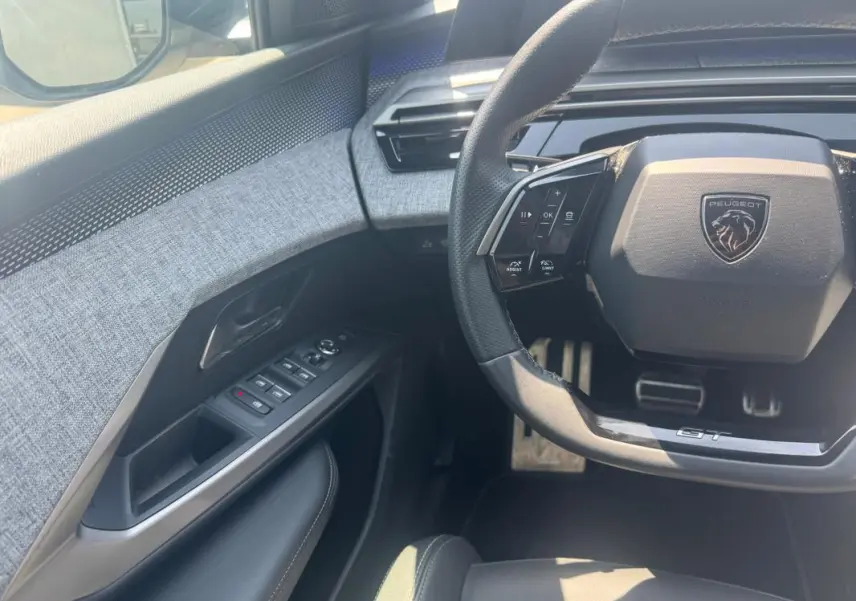 Vue intérieure côté conducteur du Peugeot 3008 Hybrid 145 e-DCS6 GT 2025, volant GT et garniture tissu gris.
