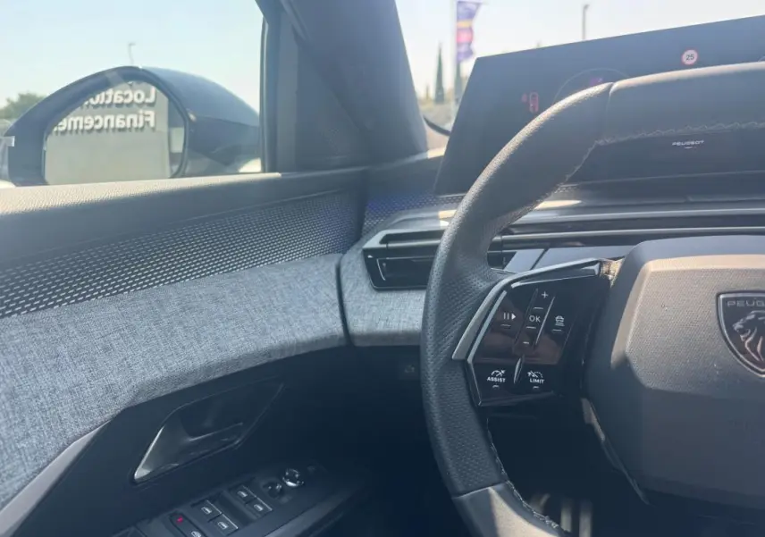 Intérieur côté conducteur du Peugeot 3008 Hybrid 145 e-DCS6 GT 2025, volant multifonction et habillage tissu gris.