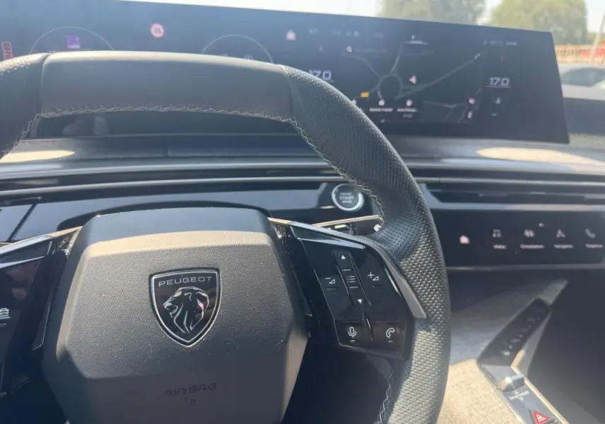 Vue intérieure centrée sur le volant noir perforé du Peugeot 3008 Hybrid 145 e-DCS6 GT avec cockpit numérique en arrière-plan.