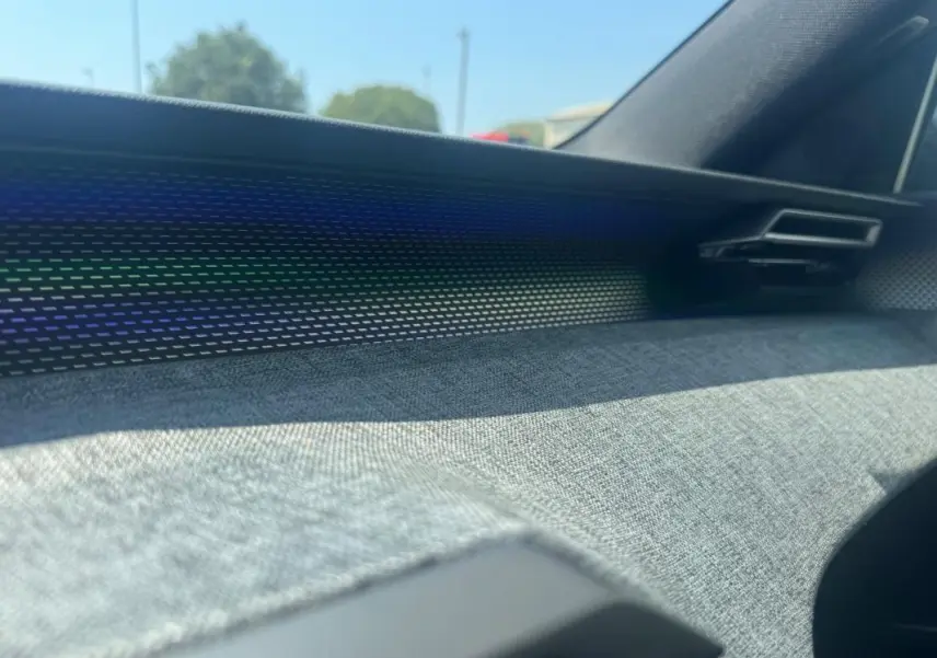 Détail de la planche de bord avec habillage tissu gris et bandeau lumineux dans un Peugeot 3008 Hybrid 145 e-DCS6 GT noir.