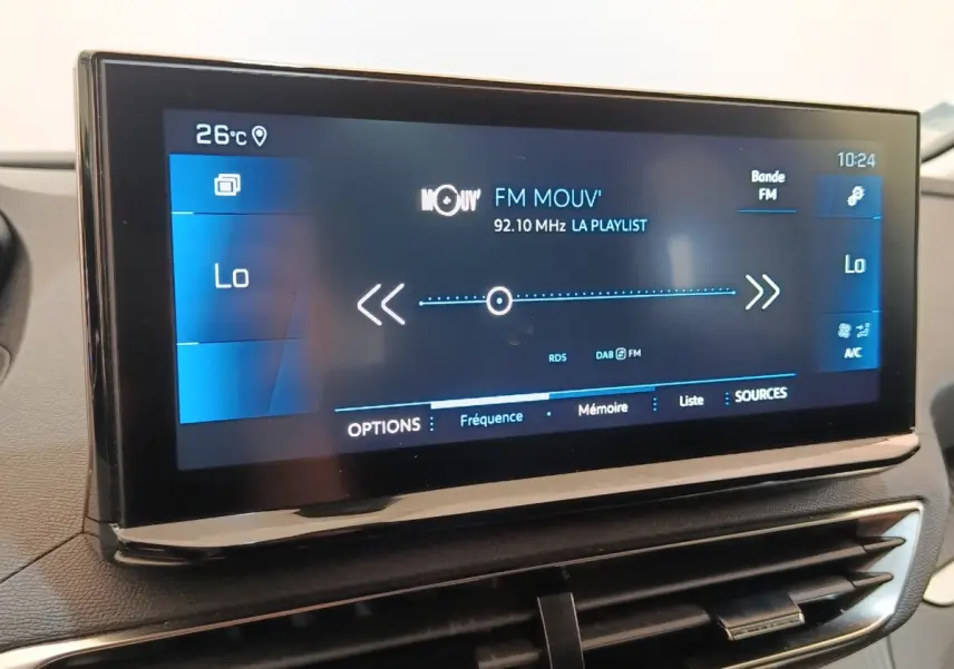 Gros plan sur l'écran tactile central du Peugeot 3008 noir, affichant la radio FM et la température intérieure à 26°C.