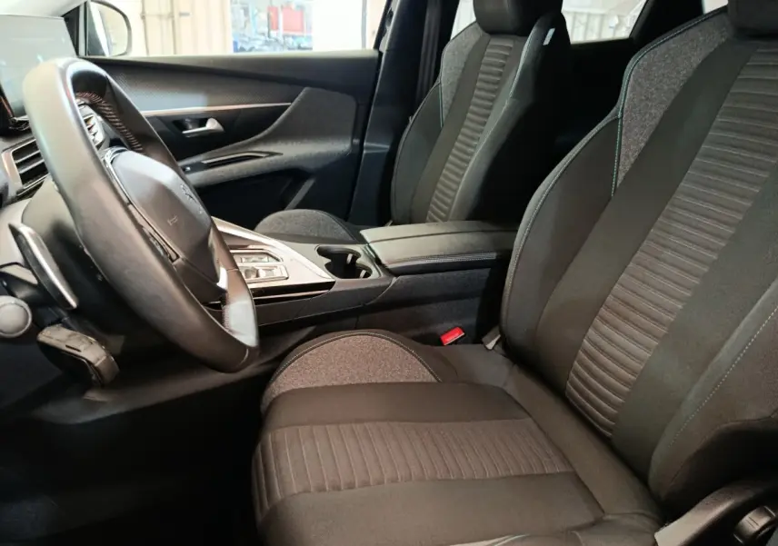 Vue intérieure côté conducteur du Peugeot 3008 noir, mettant en valeur les sièges en tissu et le volant cuir multifonctions.