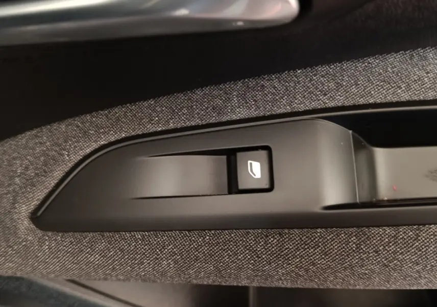 Gros plan sur le bouton de commande de lève-vitre intégré dans la garniture tissu gris côté porte d’un Peugeot 3008 noir 2022.