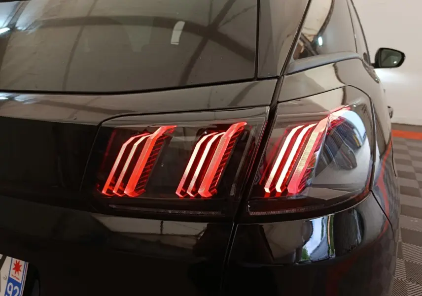Feu arrière droit allumé du Peugeot 3008 noir, vue rapprochée du coin arrière en intérieur.