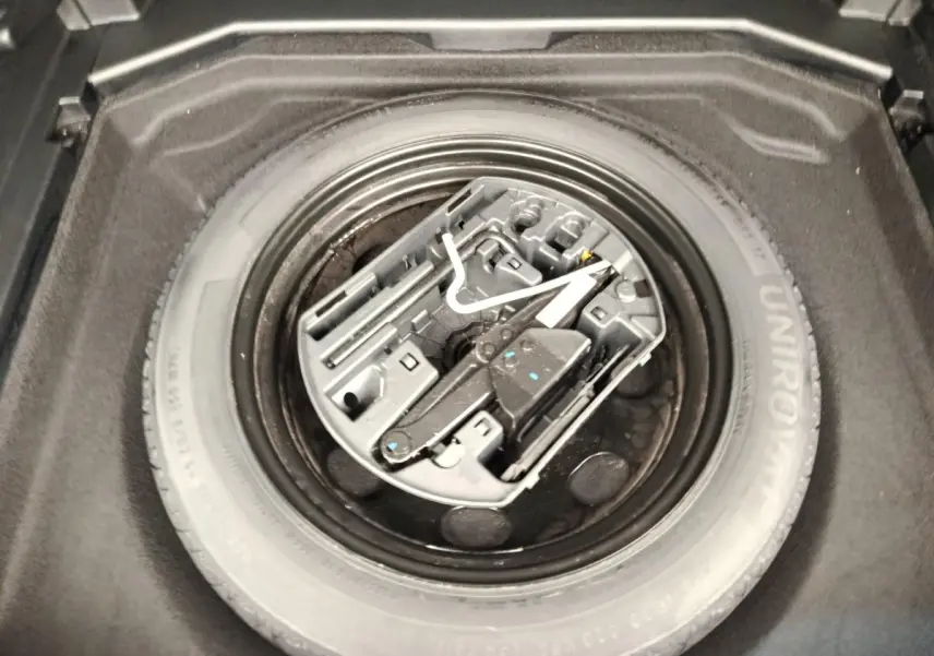 Vue plongeante sur la roue de secours noire et son kit d'outils dans le coffre du Peugeot 3008 noir 2022.