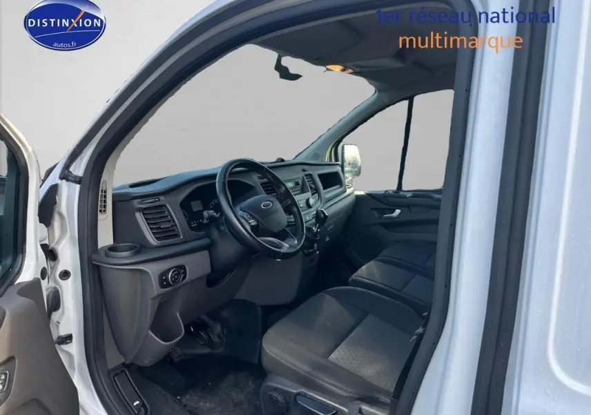 Vue intérieure côté conducteur du Ford Transit Custom blanc 2021, montrant le tableau de bord et les sièges en tissu noir.