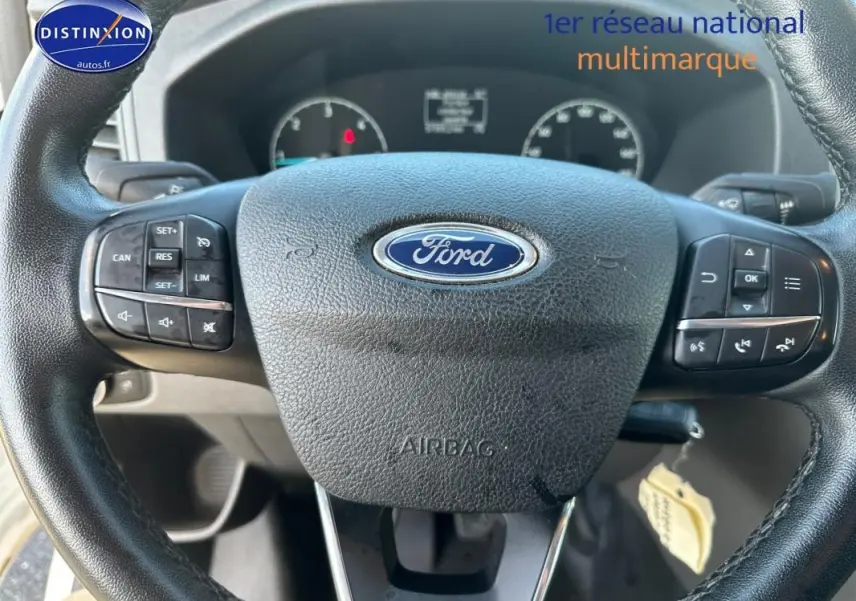 Volant cuir noir Ford avec commandes intégrées, tableau de bord partiellement visible en arrière-plan.