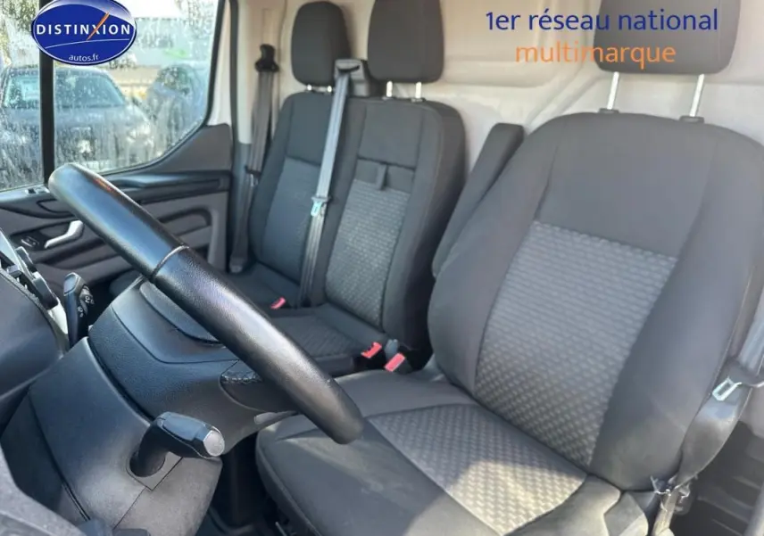 Intérieur du Ford Transit Custom blanc 2021, vue côté conducteur sur les sièges avant en tissu gris et volant cuir.