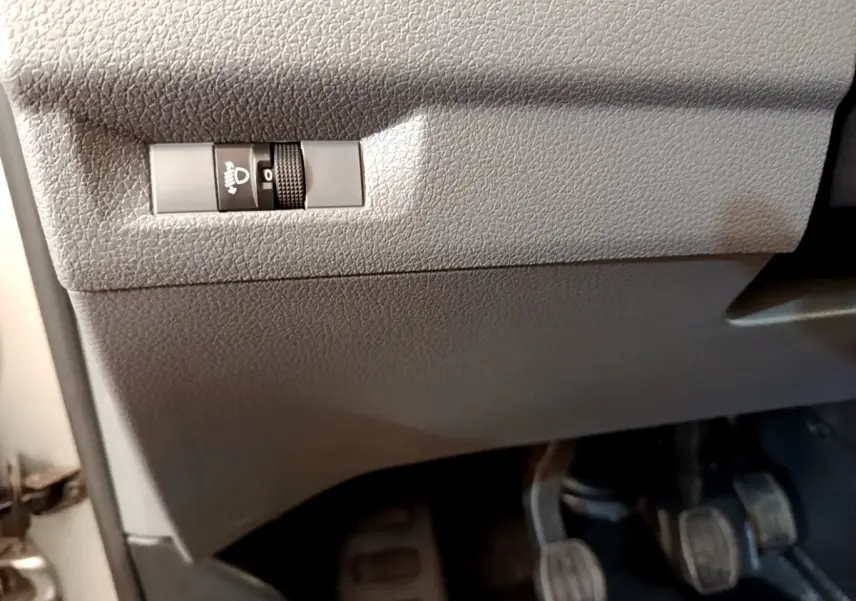 Détail du tableau de bord gris clair du Toyota Proace Verso 2019 montrant le réglage manuel des phares et les pédales côté conducteur.
