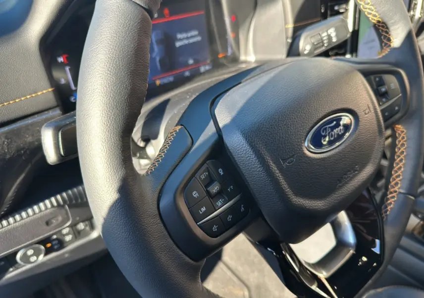 Gros plan sur le volant cuir noir avec surpiqûres marron du Ford Ranger 2025, montrant les commandes multifonctions.