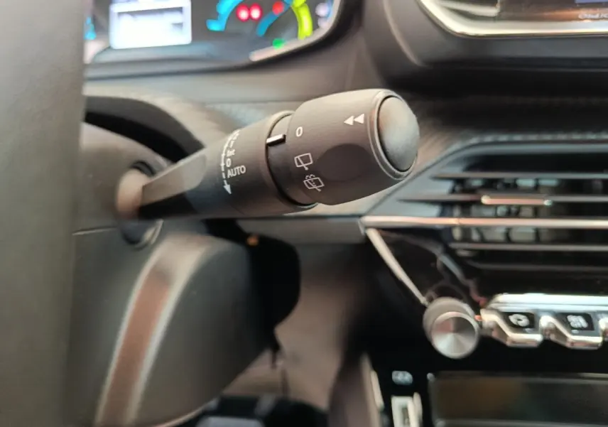 Gros plan sur la commande d’essuie-glace à gauche du volant dans l’habitacle d’une Peugeot 208 électrique blanche.