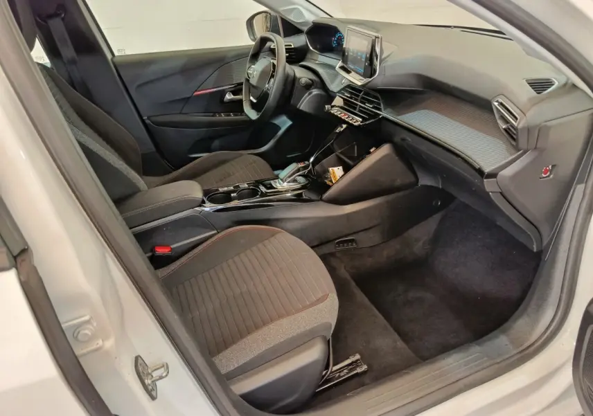 Intérieur avant droit de la Peugeot 208 électrique blanche, avec tableau de bord moderne et écran tactile central.