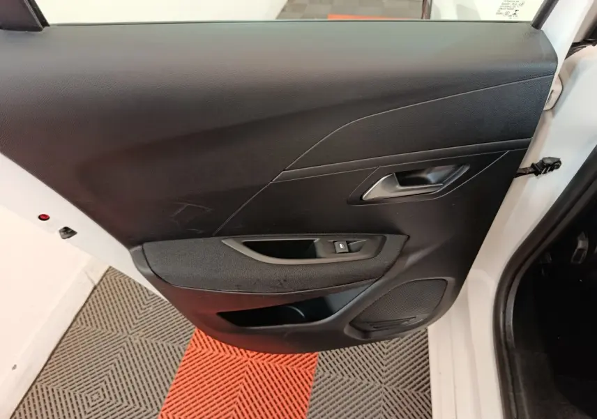 Vue intérieure de la porte arrière droite noire d'une Peugeot 208 électrique blanche, avec bouton de lève-vitre.