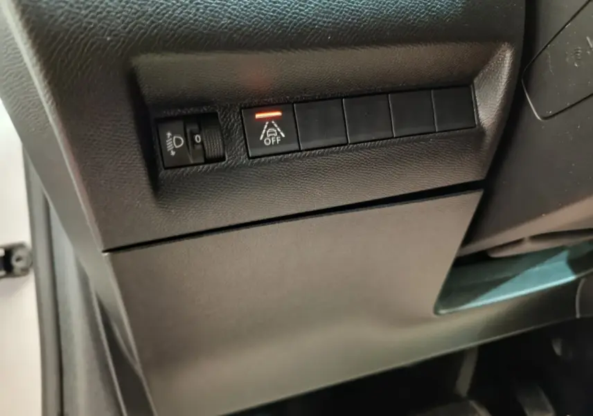 Détail intérieur du tableau de bord côté conducteur de la Peugeot 208 électrique blanche, avec commandes d’éclairage et d’aide à la conduite.