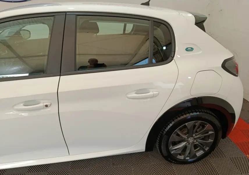 Vue latérale droite d'une Peugeot 208 électrique blanche, avec logo "e" distinctif sur l'aile arrière.