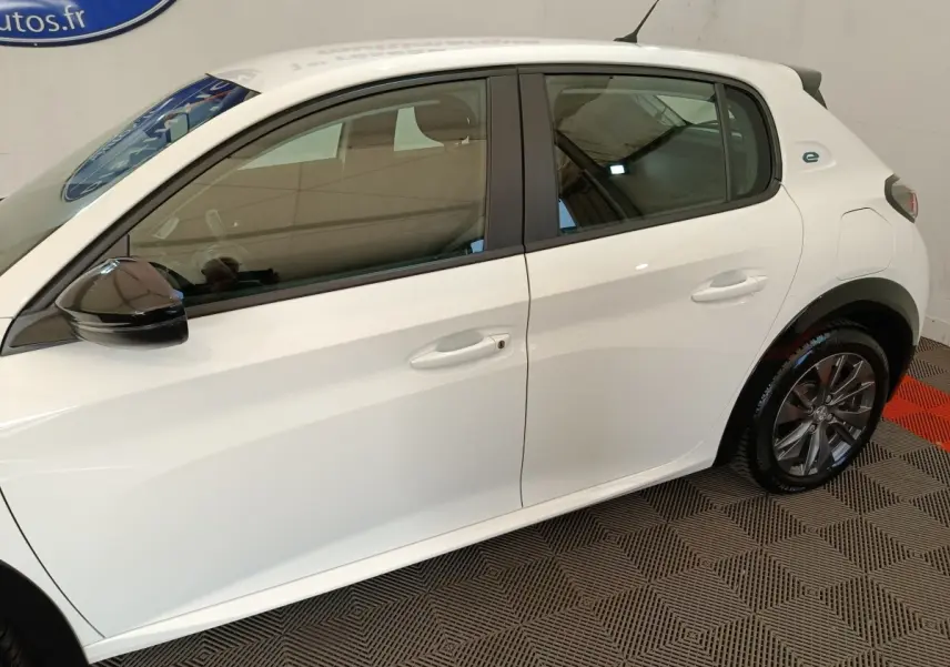 Vue latérale droite d'une Peugeot 208 électrique blanche avec rétroviseur noir et jantes alliage gris.