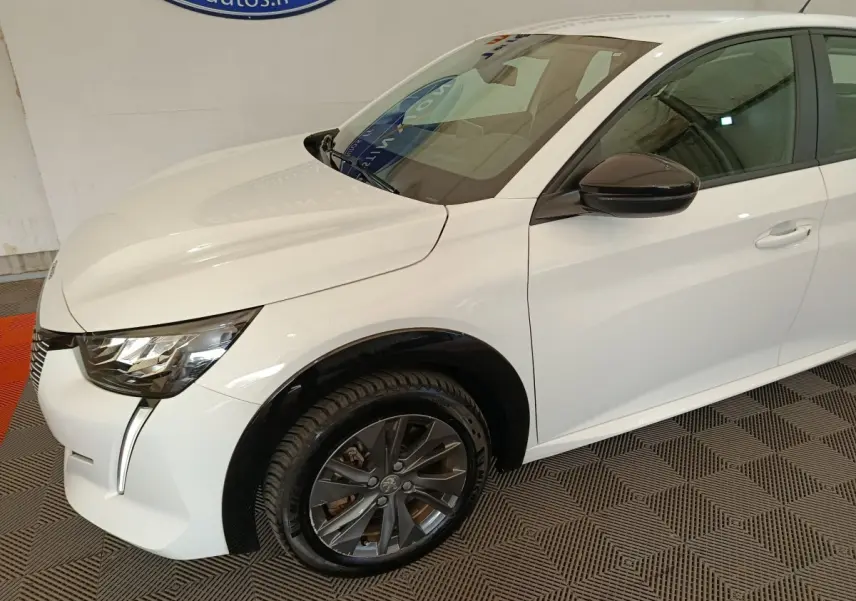 Peugeot 208 électrique blanche vue 3/4 avant droit avec jantes foncées et rétroviseur noir brillant.