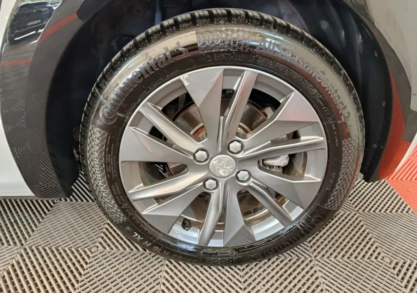 Gros plan sur la roue avant droite de la Peugeot 208 électrique blanche, avec jante alliage et pneu Continental.