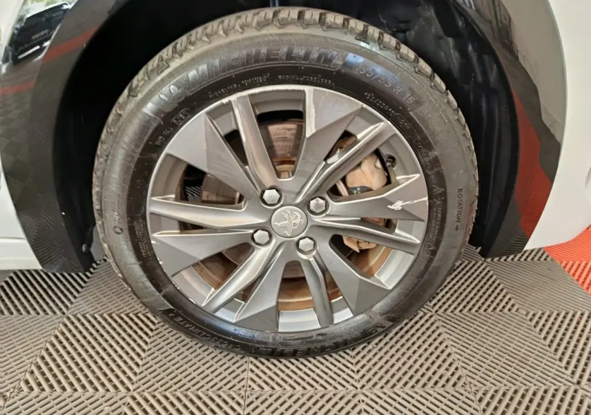 Gros plan sur la roue avant droite d'une Peugeot 208 électrique blanche avec jante alliage grise et logo lion central.