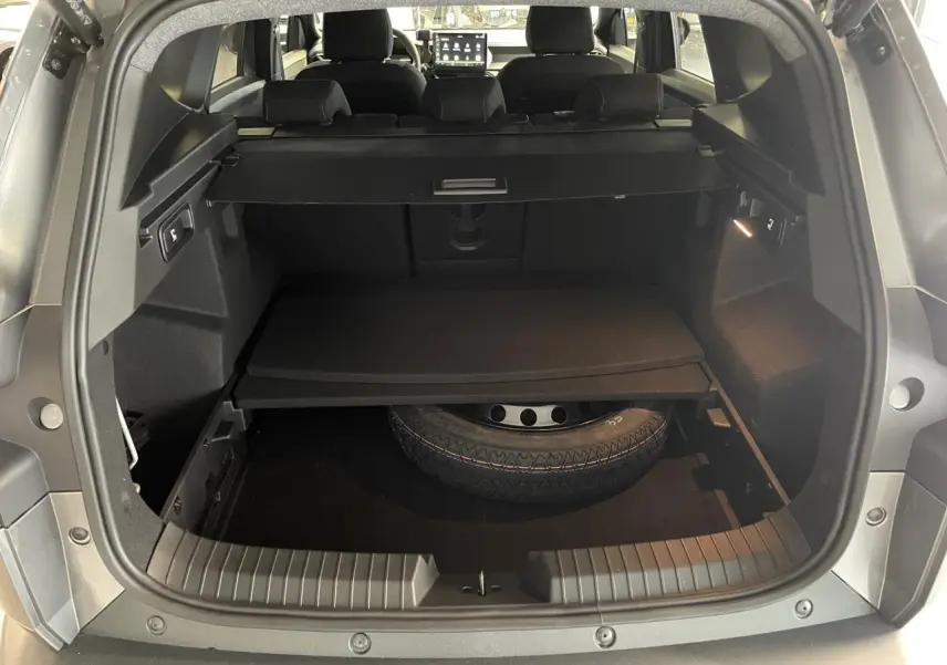 Coffre ouvert du Dacia Bigster gris schiste montrant la roue de secours galette et la banquette arrière rabattable.
