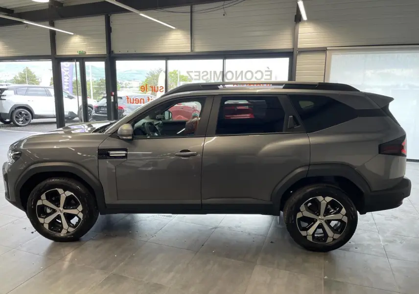 Vue de profil côté gauche du Dacia Bigster gris schiste avec jantes alliage 18 pouces diamantées en showroom.