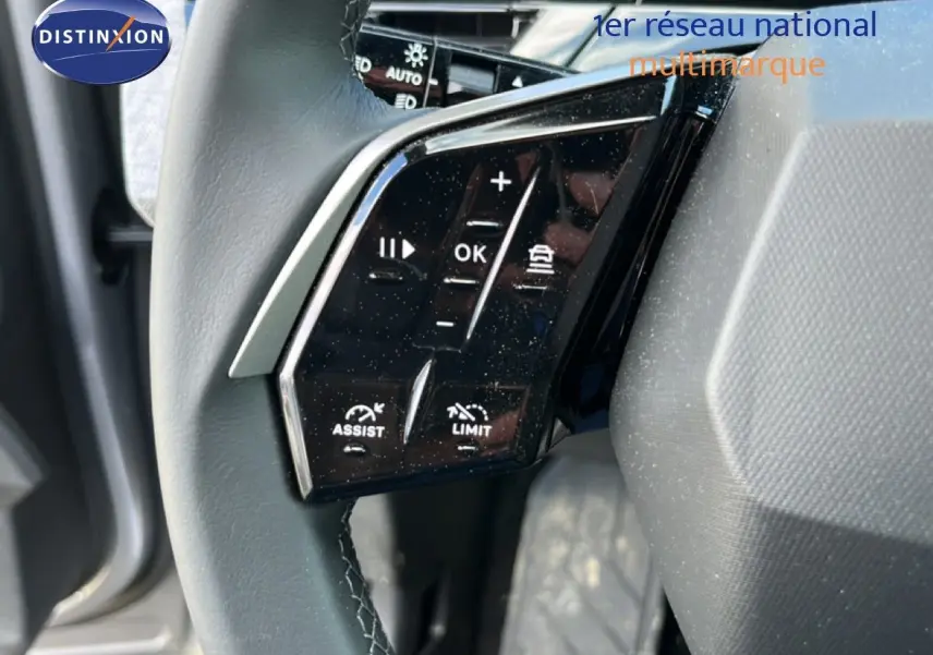 Gros plan sur les commandes du volant noir du Peugeot 5008 gris Artense, mettant en valeur les fonctions d'assistance et limiteur.