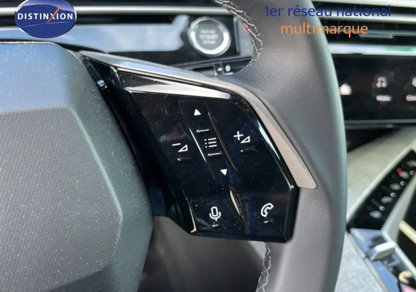 Gros plan sur les commandes gauche du volant gris cuir du Peugeot 5008 Hybrid 145ch 2025 avec tableau de bord moderne en arrière-plan.