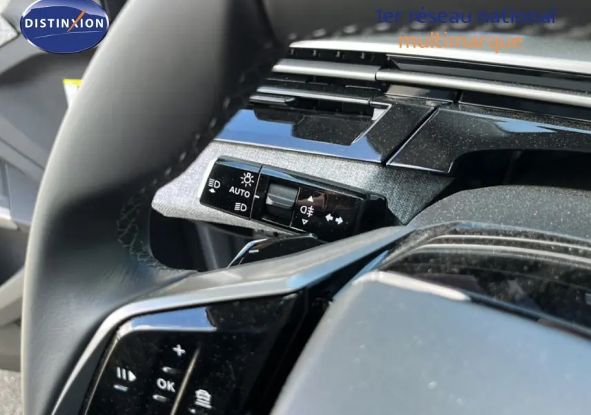 Gros plan sur le volant noir et la commande des phares du Peugeot 5008 gris Artense, intérieur moderne et soigné.