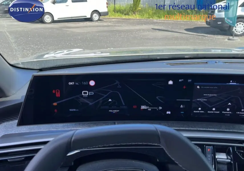 Vue intérieure centrée sur le tableau de bord numérique du Peugeot 5008 gris Artense, affichant la navigation et les informations de conduite.