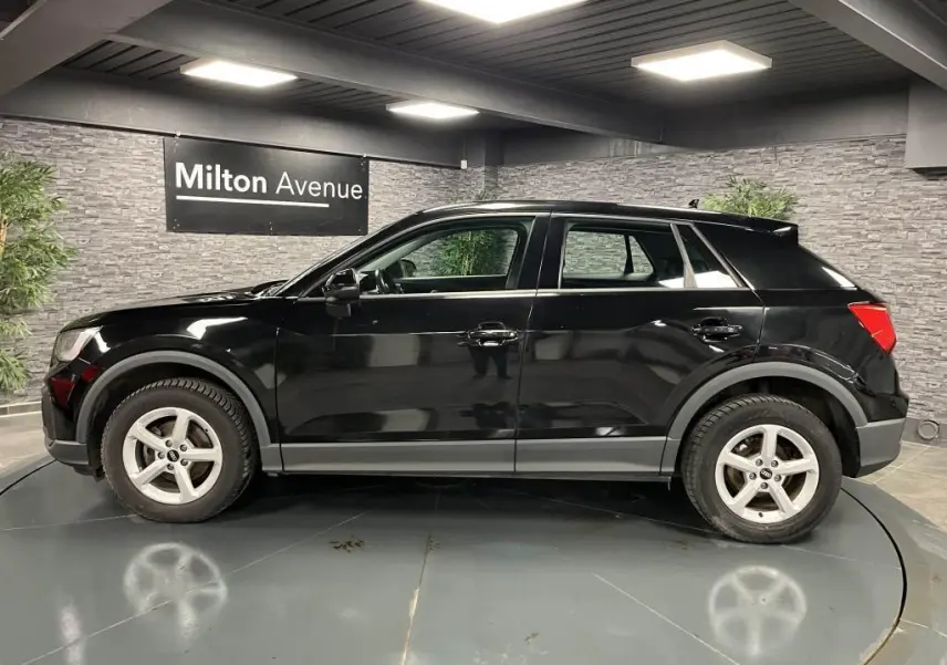 Profil côté gauche d'un Audi Q2 noir brillant 2022 avec jantes aluminium 5 branches en intérieur showroom.