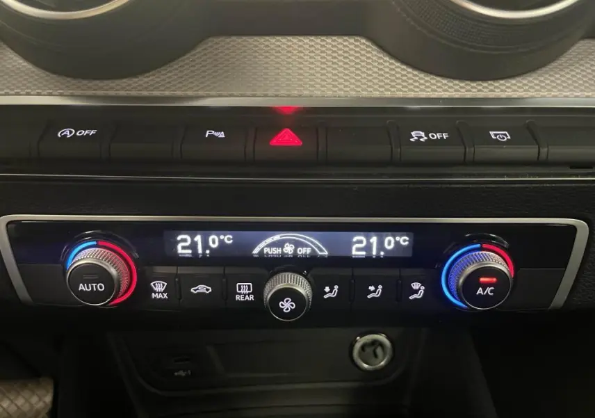 Vue rapprochée de la console centrale de l'Audi Q2 2022, affichant la climatisation automatique à 21°C avec commandes rétroéclairées.