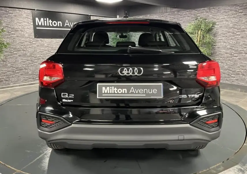 Vue arrière d'un Audi Q2 noir brillant 2022 avec feux LED et logo distinctif sur fond intérieur showroom.