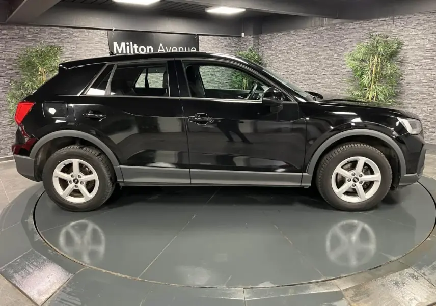Audi Q2 noir vue de profil côté gauche, avec jantes aluminium 5 branches dans un showroom intérieur.