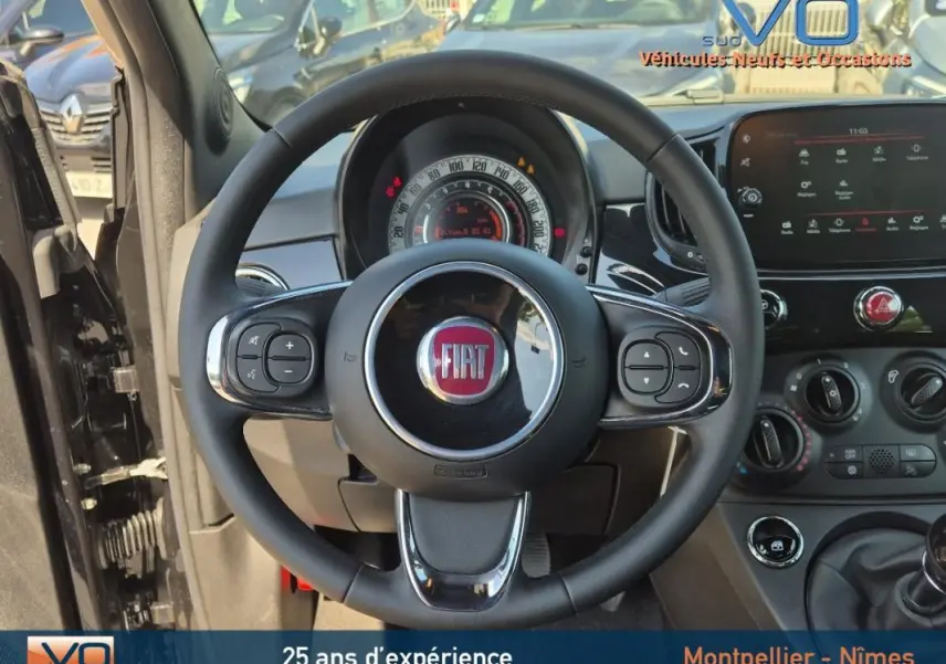 Vue intérieure centrée sur le volant de la Fiat 500C noire 2024, avec tableau de bord et commandes visibles.