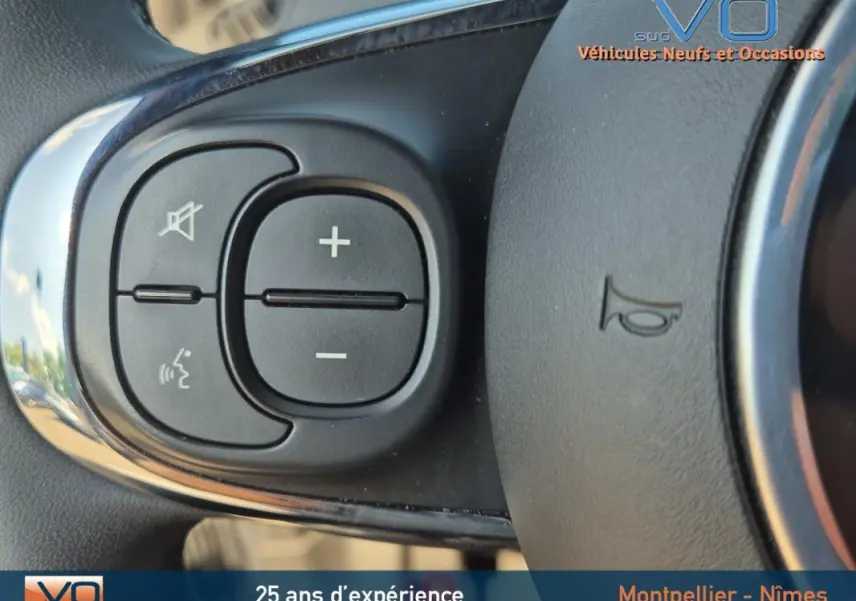 Gros plan sur les commandes de volume et de téléphone au volant d'une FIAT 500C noire 2024 hybride.