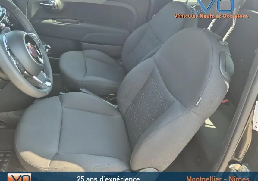 Intérieur avant du Fiat 500C noir 2024, montrant les sièges tissu gris et le volant côté gauche.