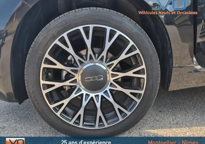 Gros plan sur la roue avant droite d'une FIAT 500C noire 2024 avec jante alliage au design étoilé.