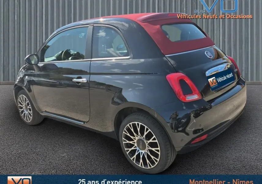 Vue 3/4 arrière droite d'une FIAT 500C noire avec toit rouge et jantes alliage distinctives, modèle 2024 hybride essence.